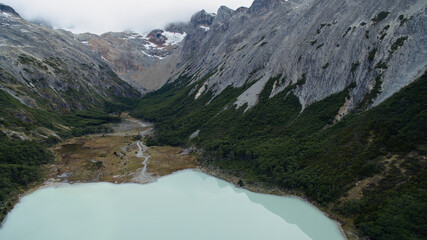 Aerial view of glacier water Emerald Lake in Ushuaia, Tierra del Fuego, Patagonia Argentina. Turquoise water lake in the Andes mountaintop surrounded by rocky mountain peaks and forrest.