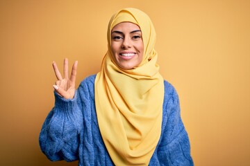 Young beautiful brunette muslim woman wearing arab hijab over isolated yellow background showing...
