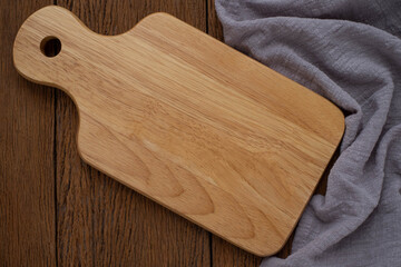 Top view above of Wooden chopping board with napkin on dark table background. Wood Cutting board with handle and hole for hanging. Empty utensil with copy space.