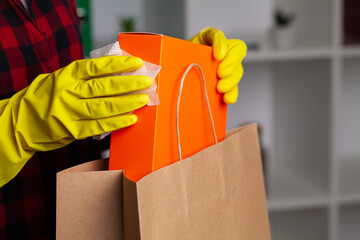 Woman in gloves disinfects product packaging at apartment