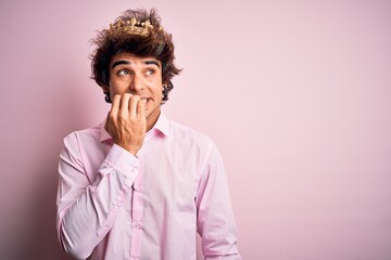Fototapeta na wymiar Young handsome man wearing king crown standing over isolated pink background looking stressed and nervous with hands on mouth biting nails. Anxiety problem.