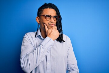 Fototapeta premium Young handsome african american man with dreadlocks wearing casual shirt and glasses with hand on chin thinking about question, pensive expression. Smiling with thoughtful face. Doubt concept.