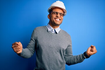 Young handsome african american engineer man with dreadlocks wearing safety helmet very happy and...