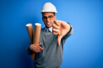 Young african american afro architect man wearing safety helmet holding bluprints with angry face,...