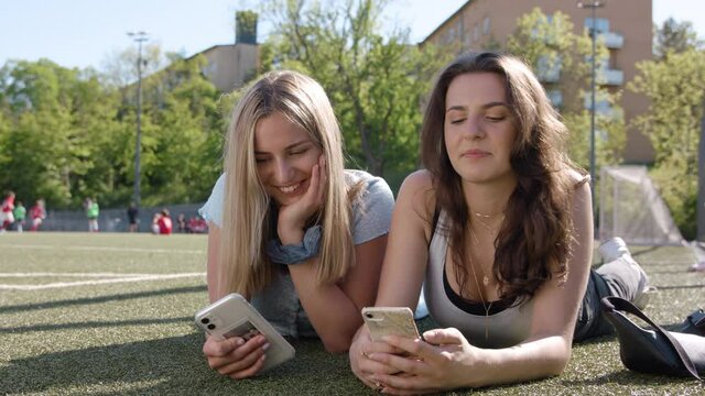 Two teenage girls taking selfies and using their smartphones.
