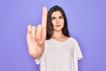 Young beautiful brunette woman wearing casual white t-shirt over purple background Pointing with finger up and angry expression, showing no gesture