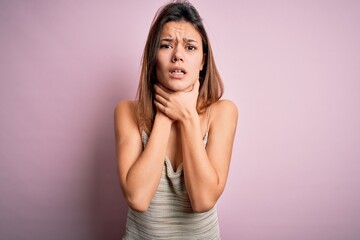 Young beautiful brunette girl wearing casual striped t-shirt over isolated pink background shouting and suffocate because painful strangle. Health problem. Asphyxiate and suicide concept.