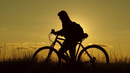 Fototapeta na wymiar woman cyclist overcomes an obstacle. Healthy young woman tourist goes with bicycle along hillside, enjoying nature, fresh air. free girl travels with bicycle in sunset. adventure and travel concept.