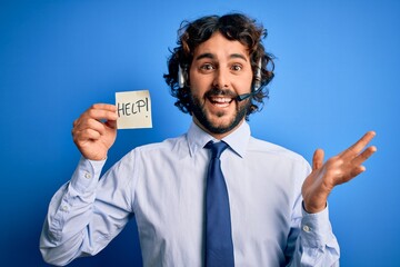 Young handsome call center agent man with beard working using headset holding help reminder very happy and excited, winner expression celebrating victory screaming with big smile and raised hands