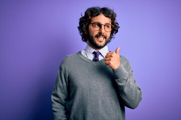 Handsome businessman with beard wearing tie and glasses standing over purple background smiling with happy face looking and pointing to the side with thumb up.