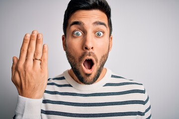 Handsome man with beard showing alliance ring marriage on finger over white background scared in shock with a surprise face, afraid and excited with fear expression