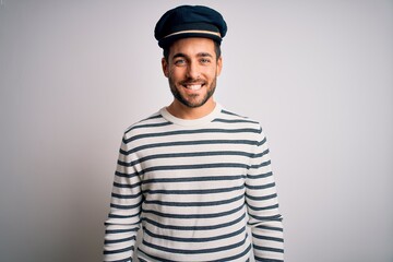 Young handsome sailor man with beard wearing navy striped uniform and captain hat with a happy and cool smile on face. Lucky person. - obrazy, fototapety, plakaty