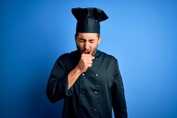 Young handsome chef man with beard wearing cooker uniform and hat over blue background feeling...
