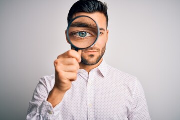 Young detective man looking through magnifying glass over isolated background with a confident...