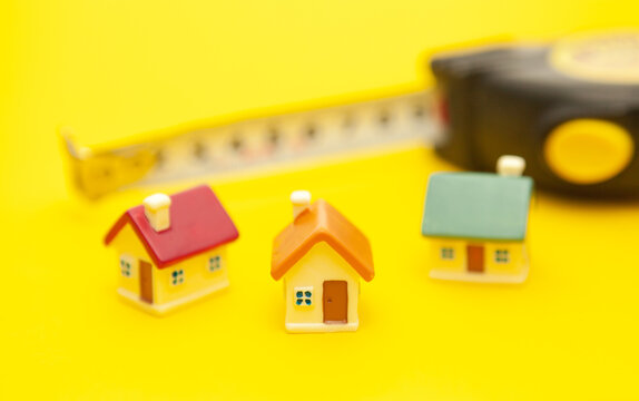 Building tape measure and colored miniature houses on a yellow background, the concept of construction of houses and cities