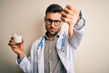 Young doctor man wearing stethoscope holding a glass of milk over isolated background with angry face, negative sign showing dislike with thumbs down, rejection concept