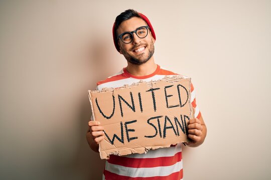 Handsome activist man protesting wearing glasses holding cardboard with unity message with a happy face standing and smiling with a confident smile showing teeth