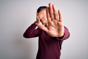 Young handsome hispanic man wearing casual shirt standing over white isolated background covering eyes with hands and doing stop gesture with sad and fear expression. Embarrassed and negative concept.