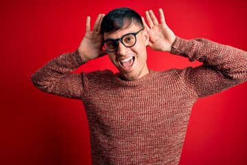 Young handsome hispanic man wearing nerd glasses over red background Smiling cheerful playing peek...