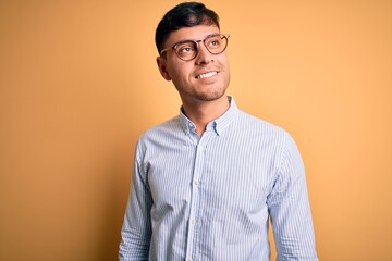 Young handsome hispanic business man wearing nerd glasses over yellow background looking away to...