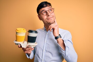 Young scholarship holder business man holding take away coffee over isolated yellow background...