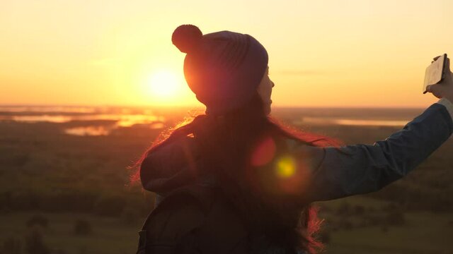 Free Young girl tourist blogger records a selfie video on top of the mountains using a smartphone with beautiful landscape. Healthy cheerful woman travels at dawn and photography nature on phone.