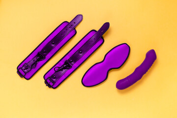 Sex toys handcuffs, sleeping mask and vibrator on bright yellow background. Sex and pleasure concept.