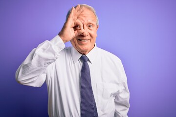 Grey haired senior business elegant man standing over purple isolated background doing ok gesture with hand smiling, eye looking through fingers with happy face.