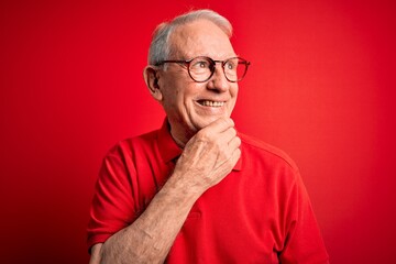 Obraz premium Grey haired senior man wearing glasses and casual t-shirt over red background with hand on chin thinking about question, pensive expression. Smiling with thoughtful face. Doubt concept.