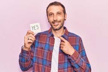 Young handsome man holding yes reminder smiling happy pointing with hand and finger