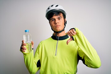 Young handsome cyclist man wearing security bike helmet drinking bottle of water with angry face, negative sign showing dislike with thumbs down, rejection concept