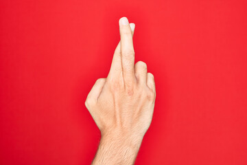 Hand of caucasian young man showing fingers over isolated red background gesturing fingers crossed, superstition and lucky gesture, lucky and hope expression