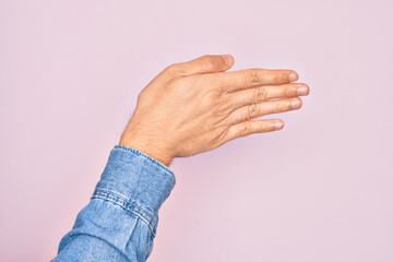 Hand of caucasian young man showing fingers over isolated pink background stretching and reaching with open hand for handshake, showing back of the hand