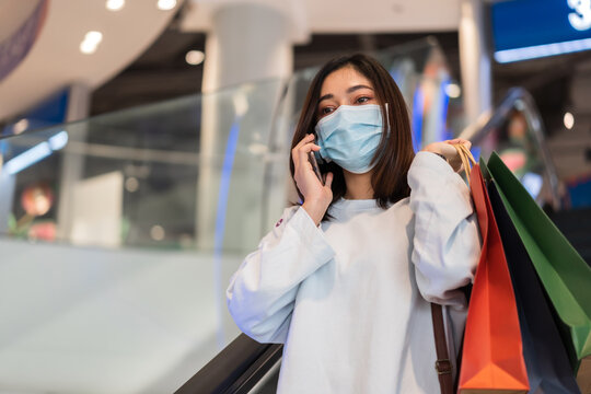 woman talking with mobile phone in shopping mall and wearing face mask protective for spreading of coronavirus(covid-19) pandemic, new normal concept