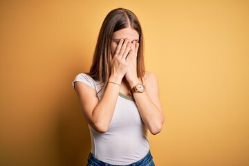 Young beautiful redhead woman wearing casual t-shirt over isolated yellow background with sad expression covering face with hands while crying. Depression concept.