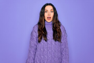 Young beautiful woman wearing casual turtleneck sweater standing over purple background In shock face, looking skeptical and sarcastic, surprised with open mouth