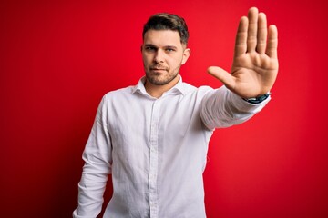Young business man with blue eyes wearing elegant shirt standing over red isolated background doing...