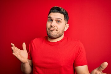 Young man with blue eyes wearing casual t-shirt over red isolated background clueless and confused...