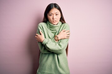 Fototapeta premium Young beautiful asian woman wearing green winter sweater over pink solated background shaking and freezing for winter cold with sad and shock expression on face