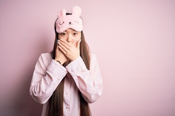 Young asian woman wearing pajama and sleep mask over pink isolated background shocked covering mouth with hands for mistake. Secret concept.
