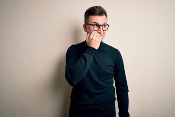 Young handsome caucasian man wearing glasses and casual sweater over isolated background looking stressed and nervous with hands on mouth biting nails. Anxiety problem.