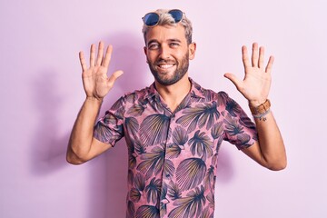 Fototapeta premium Handsome blond man on vacation wearing casual shirt and sunglasses over pink background showing and pointing up with fingers number ten while smiling confident and happy.