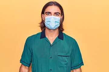 Young handsome man wearing medical mask with serious expression on face. simple and natural looking at the camera.