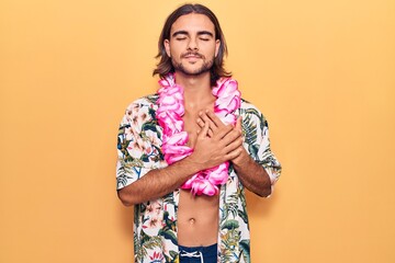 Young handsome man wearing swimwear and hawaiian lei smiling with hands on chest with closed eyes...