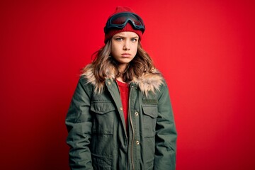 Young blonde girl wearing ski glasses and winter coat for ski weather over red background skeptic and nervous, frowning upset because of problem. Negative person.