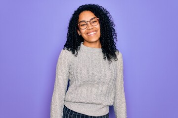Young african american woman wearing casual sweater and glasses over purple background winking looking at the camera with sexy expression, cheerful and happy face.
