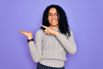 Young african american woman wearing casual sweater and glasses over purple background amazed and smiling to the camera while presenting with hand and pointing with finger.