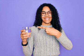 Young african american woman drinking glass of water over isolated purple background very happy...