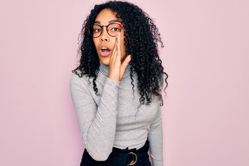 Young african american woman wearing turtleneck sweater and glasses over pink background hand on mouth telling secret rumor, whispering malicious talk conversation