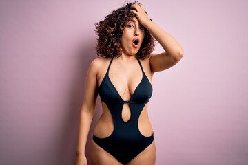 Young beautiful arab woman on vacation wearing swimsuit and sunglasses over pink background...